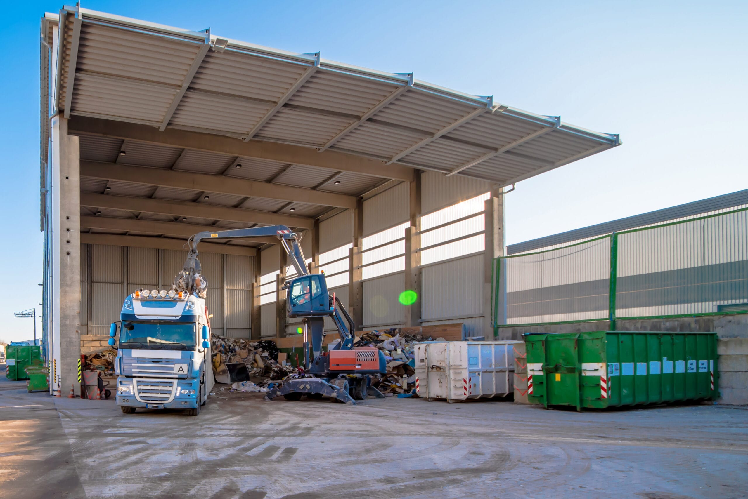 A truck sorting waste under a outdoor canopy at a recycling center