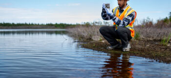 Marine biologist crouches at edge of river analysing water test results and algea samples