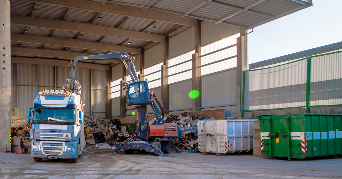 A truck sorting waste under a outdoor canopy at a recycling center