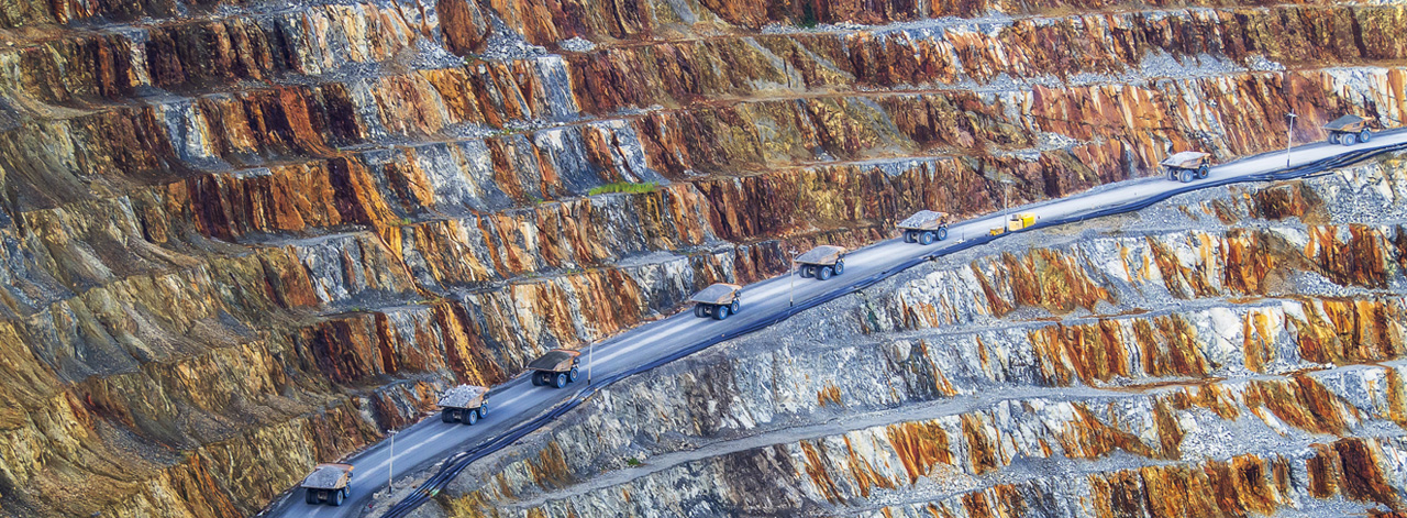 Strip mining background with a road running parallel and multiple trunks driving on road
